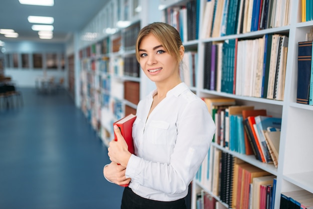 Jeune femme avec livre pose sur l'étagère de la bibliothèque.