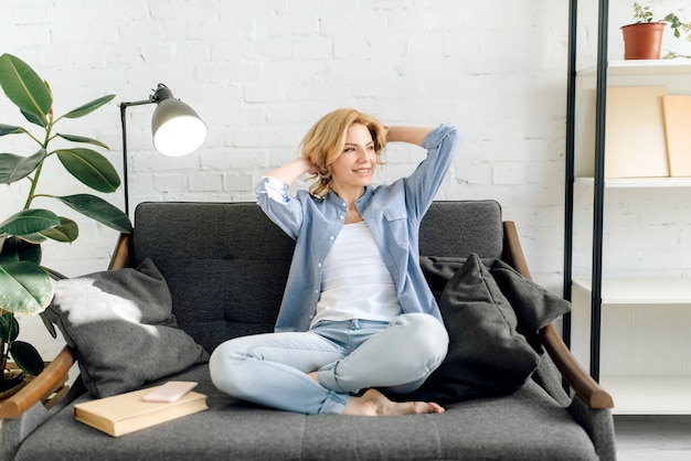 Jeune femme avec livre s'étirer sur un canapé confortable