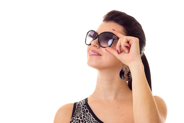 Jeune femme avec une longue queue de cheval et de grandes boucles d'oreilles en maillot de bain noir tenant des lunettes de soleil noires