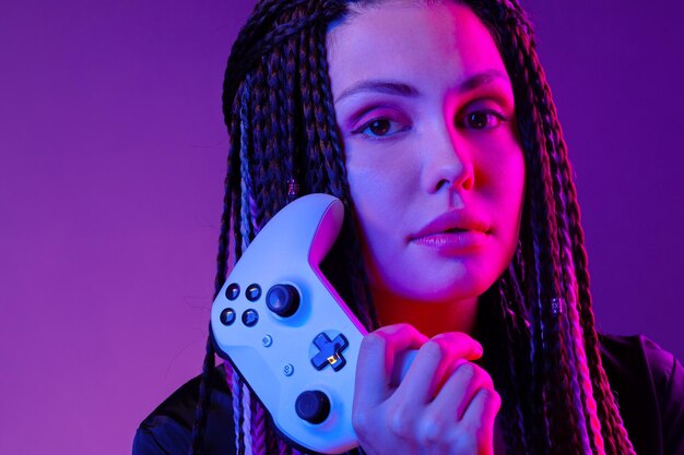 Jeune femme avec de longues tresses tenant le joystick de la console sur fond violet foncé