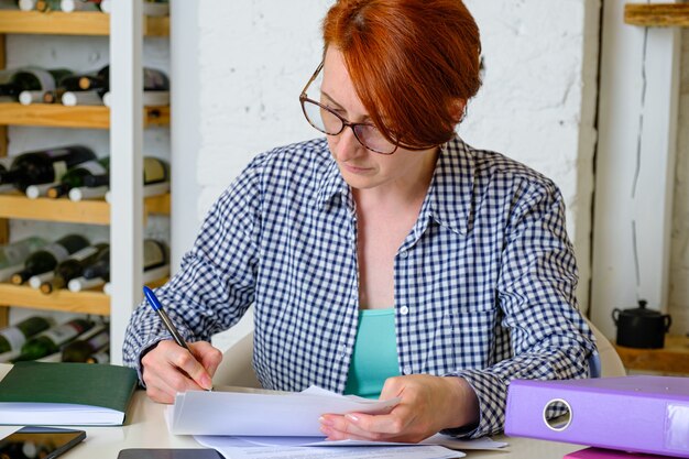 Jeune femme avec des lunettes aux cheveux courts rouges travaille avec des documents au bureau