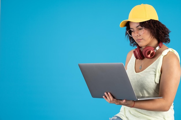 Jeune femme avec des lunettes et une casquette à l'aide d'un ordinateur portable sur sa main et son casque