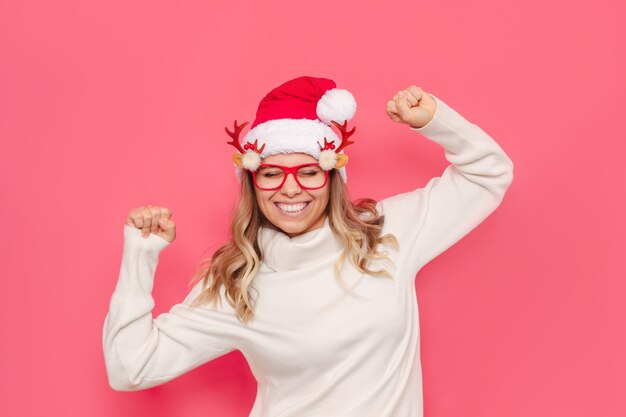 Jeune femme à lunettes avec chandail de bois de cerf Noël Santa hat est heureux avec ses mains vers le haut