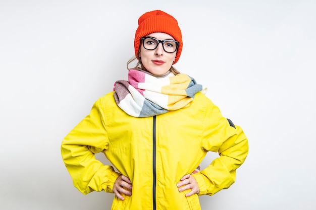 Jeune femme à lunettes dans une veste jaune tenant ses mains sur sa taille sur un fond clair.