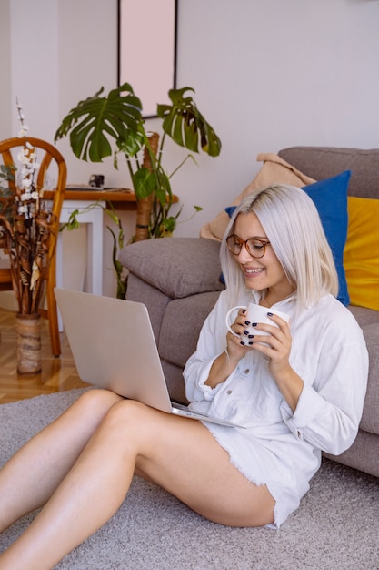 Jeune femme à lunettes faisant des travaux de recherche pour son entreprise tout en prenant son petit déjeuner à la maison