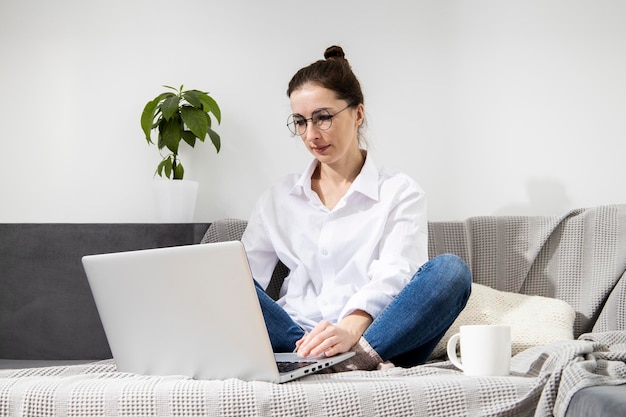 Jeune femme à lunettes avec ordinateur portable avec café assis sur un canapé