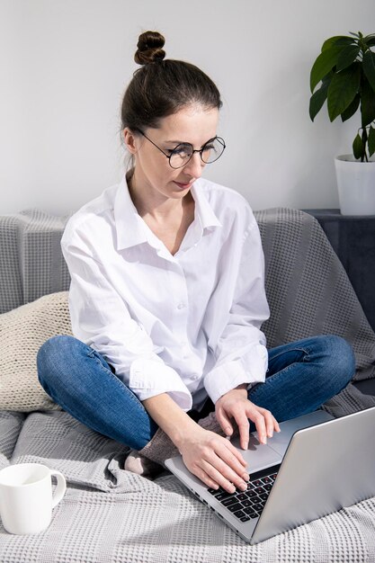 Jeune femme à lunettes avec ordinateur portable avec café assis sur un canapé