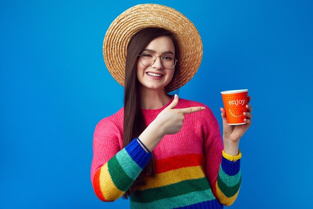 Jeune femme avec des lunettes pointe au café à emporter a une expression joyeuse