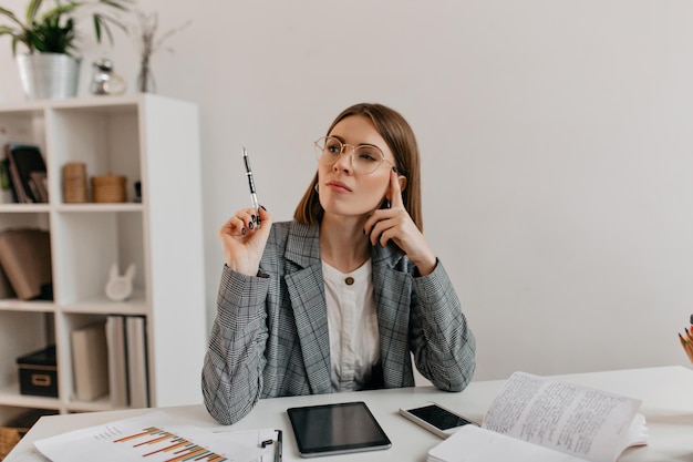 Jeune femme à lunettes a réfléchi à une nouvelle idée d'entreprise tout en travaillant dans un bureau blanc