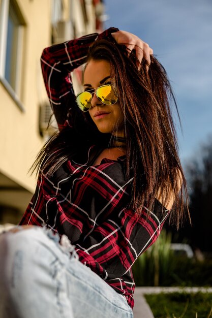 Photo une jeune femme avec des lunettes de soleil assise contre le bâtiment