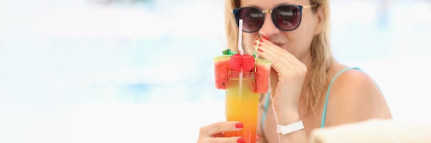 Jeune femme à lunettes de soleil buvant un cocktail alcoolisé multicolore sur la plage