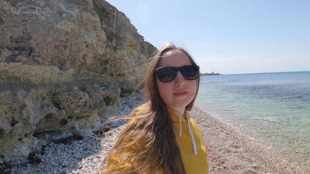 Une jeune femme à lunettes de soleil se filme au bord de la mer. Repos à la mer. Blog de voyage. 4K UHD