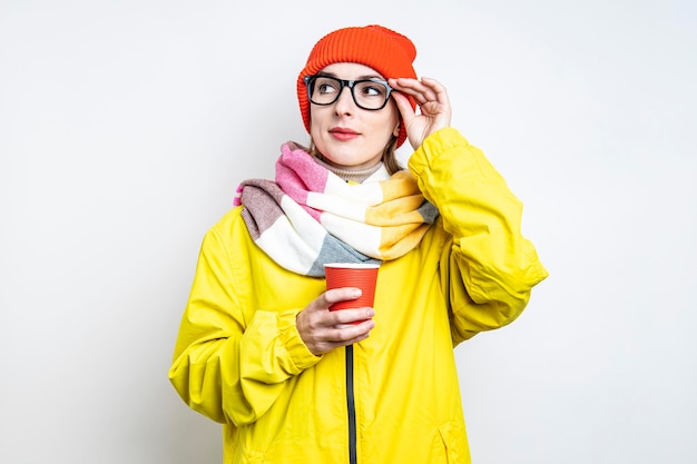 Jeune femme à lunettes avec une tasse de papier sur un fond clair.