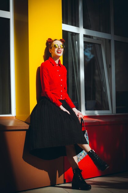 Jeune femme à lunettes et une veste rouge contre un mur jaune