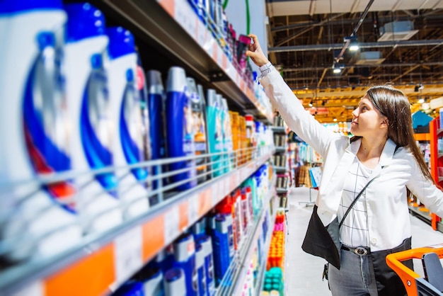 Jeune femme en magasin avec chariot choisir shampooing dans l'espace de copie de concept de magasinage de supermarché