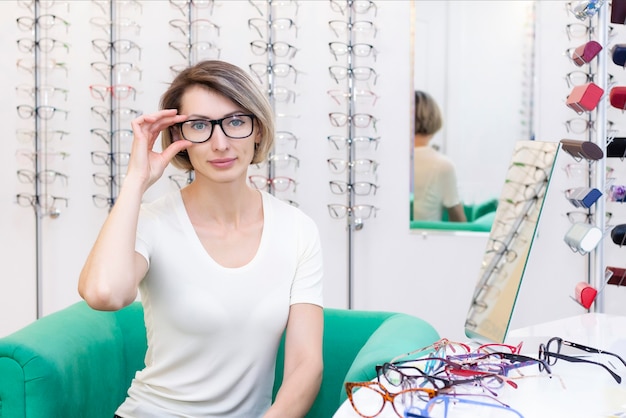 Jeune femme en magasin d'optique choisissant de nouvelles lunettes avec un opticien. lunettes dans le magasin d'optique. Une femme choisit des lunettes. Émotions. Ophtalmologie.