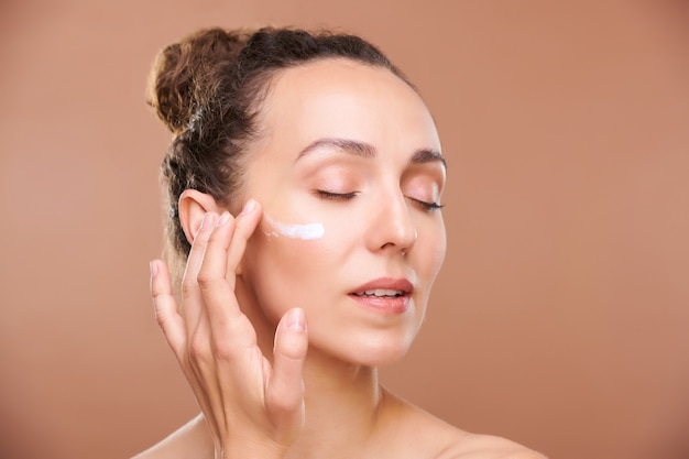 Jeune femme magnifique appliquant une crème ou un sérum pour le visage sur la zone sous les yeux tout en prenant soin de sa peau le matin ou avant de dormir