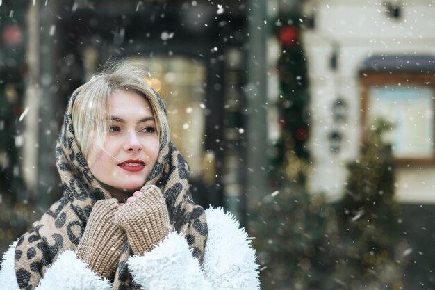 Une jeune femme magnifique porte une écharpe chaude marchant dans la ville pendant les chutes de neige. Espace libre