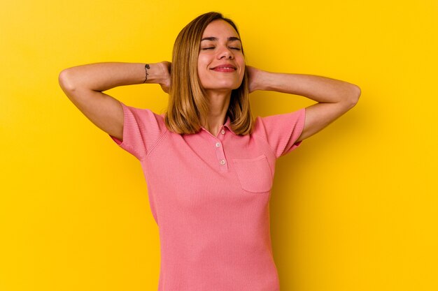 Jeune femme maigre caucasienne isolée sur jaune se sentant confiant, avec les mains derrière la tête.