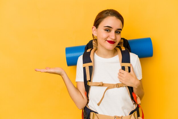 Jeune femme maigre voyageur arabe montrant un espace de copie sur une paume et tenant une autre main sur la taille.