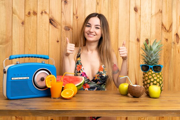 Jeune femme en maillot de bain avec beaucoup de fruits donnant un geste du pouce levé