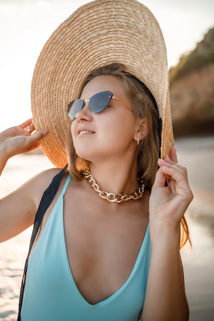 Jeune femme en maillot de bain et un chapeau au bord de la mer à la lumière du coucher du soleil. Concept de vacances d'été. Mise au point sélective