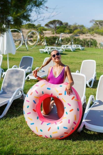 Une jeune femme en maillot de bain élégant et lunettes de soleil tient un anneau de beignet gonflable dans sa main. Belle fille heureuse posant et s'amusant au soleil. Vacances. voyager