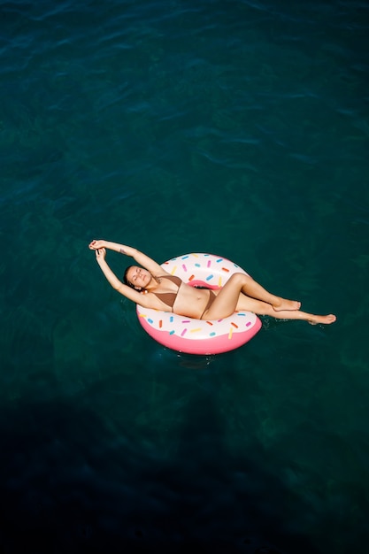 Jeune femme en maillot de bain nage sur un anneau gonflable dans la mer. Concept de vacances d'été.