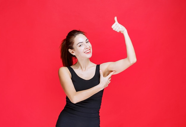 Jeune femme en maillot noir debout sur le mur rouge et montrant le pouce vers le haut