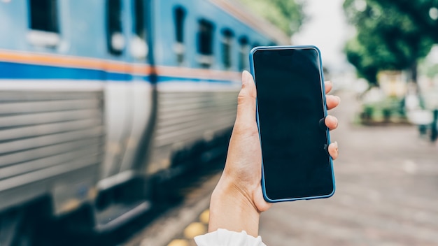 Jeune femme mains tenant mobile à la gare pour la recherche de chambre d'hôtel pour la réservation et le paiement par internet sans numéraire.