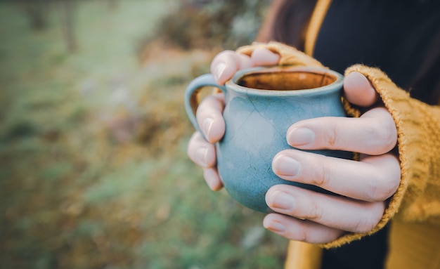 Jeune femme mains tenant une tasse bleue de thé concept saisonnier en plein air copyspace