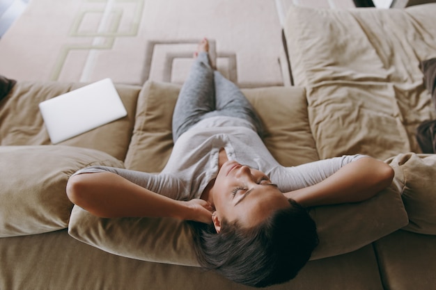 Photo la jeune femme à la maison allongée sur le canapé et se reposant dans son salon les mains sous la tête