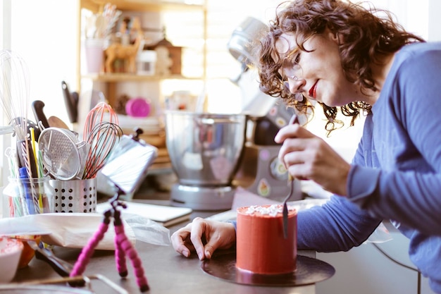 Jeune femme à la maison enseignant un cours de pâtisserie en ligne. Elle utilise un téléphone portable sur un trépied. Blog culinaire.