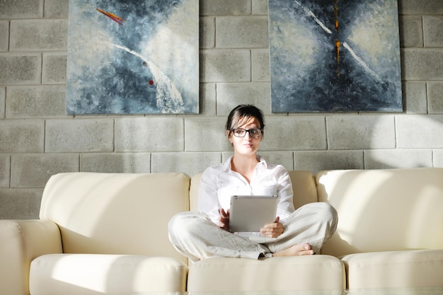Jeune femme à la maison se détendre dans son salon en lisant une tablette numérique surfer sur Internet et travailler