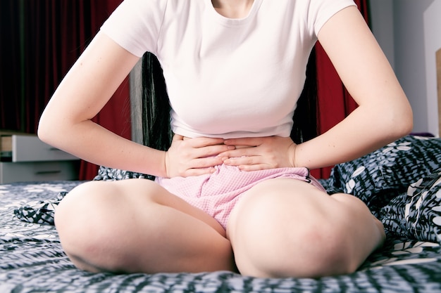 Une jeune femme a mal au ventre alors qu'elle est assise sur le lit