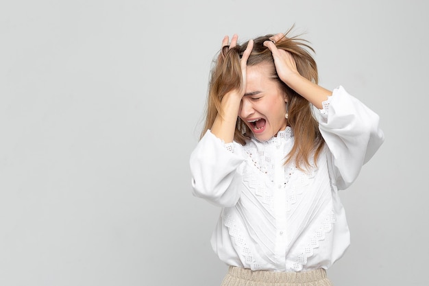 Jeune femme avec un mal de tête tient sa tête isolée sur un fond gris blanc la femme souffre beaucoup de douleur