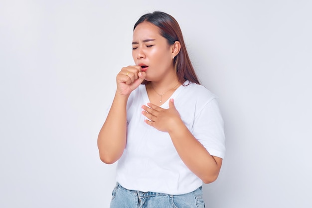 Jeune femme malade asiatique portant un t-shirt blanc décontracté couvrant la bouche avec une toux éternuée isolée sur fond blanc concept de mode de vie des gens