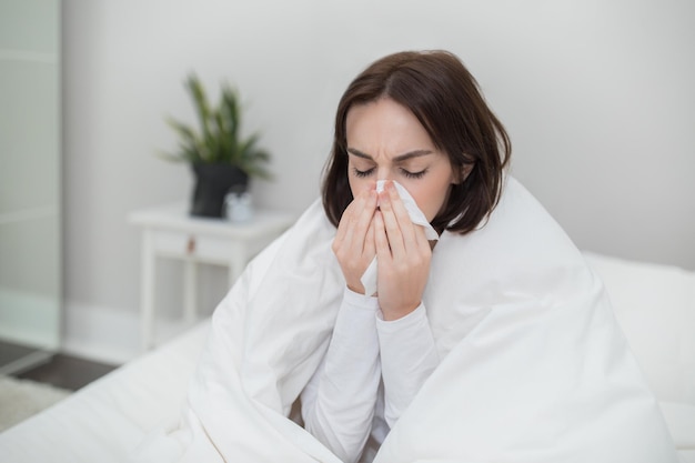 Jeune femme malade éternue en restant au lit à la maison