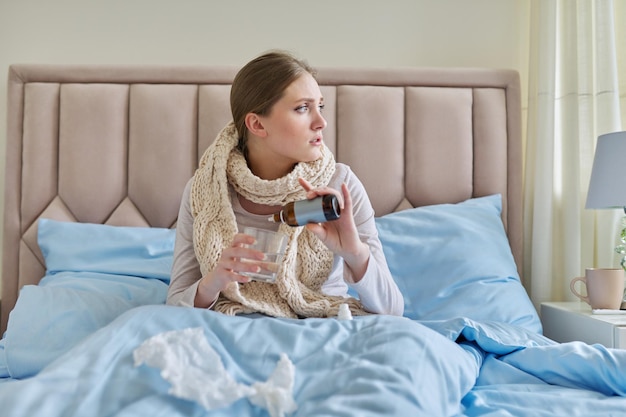 Jeune femme malade à la maison au lit femme tenant un verre d'eau et des gouttes de médecine