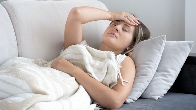 Jeune femme malade avec mal de tête allongée sur un canapé dans le salon