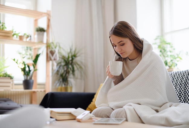 Jeune femme malade et malade avec une couverture buvant du thé à la maison, concept de coronavirus.