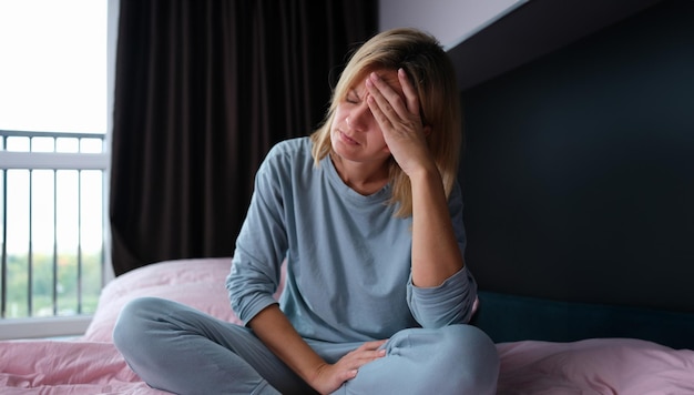 Jeune femme malade en pyjama assise dans son lit et tenant sa tête