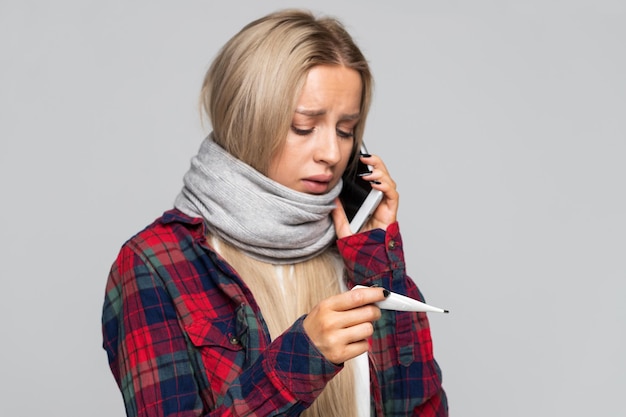 Photo une jeune femme malade qui regarde le thermomètre et parle au téléphone a des symptômes de grippe.