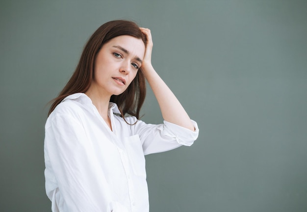 Jeune femme malheureuse aux cheveux longs en chemise blanche sur fond gris émotion négative