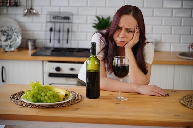 Une jeune femme malheureuse a mal à la tête à cause du vin rouge Une femme adulte se sent mal à cause de l'alcool dans la cuisine