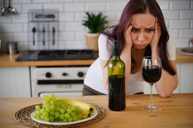 Une jeune femme malheureuse a mal à la tête à cause du vin rouge Une femme adulte se sent mal à cause de l'alcool dans la cuisine