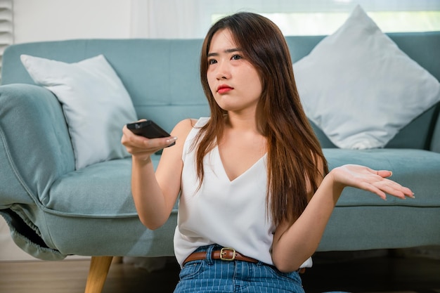 Une jeune femme malheureuse regarde un film à la télévision à la maison, s'ennuie belle femme tenant la télécommande de la télévision assise sur le sol du canapé dans le salon à la maison, ennuyeuse avec le programme de télévision