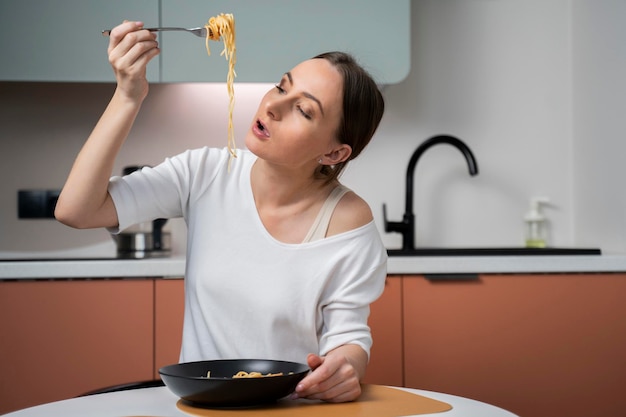 Une jeune femme mange de délicieux pâtes tout en appréciant un délicieux déjeuner fait maison assise à une table