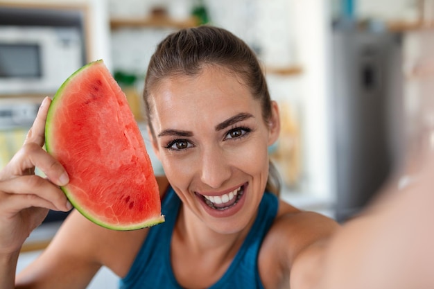 Jeune femme mange une tranche de pastèque dans la cuisine Portrait de jeune femme appréciant une pastèque