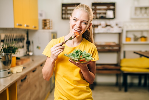 Jeune femme mangeant dans la cuisine, des aliments écologiques sains.